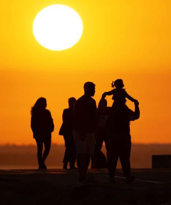 Black silhouettes of people walking on the hill at bright orange sunset